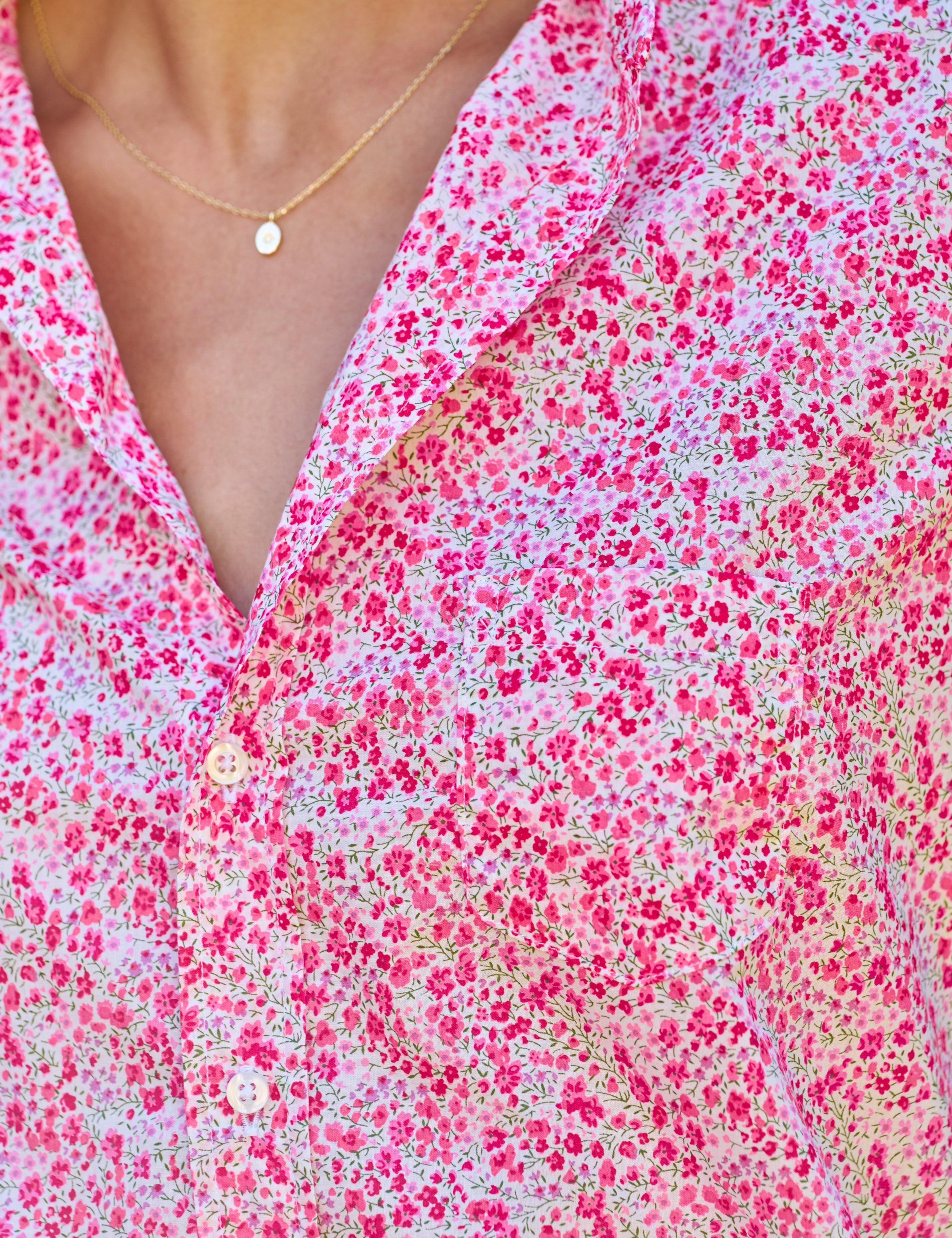 Close-up of a person wearing a pink floral dress with a necklace.
