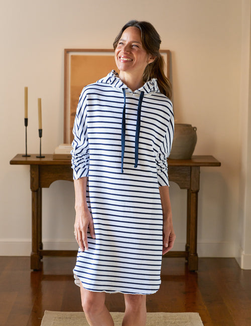 Woman wearing a blue and white striped dress standing in a room with wooden furniture., front view