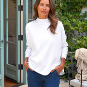 Woman wearing a white sweater and blue pants standing outdoors.