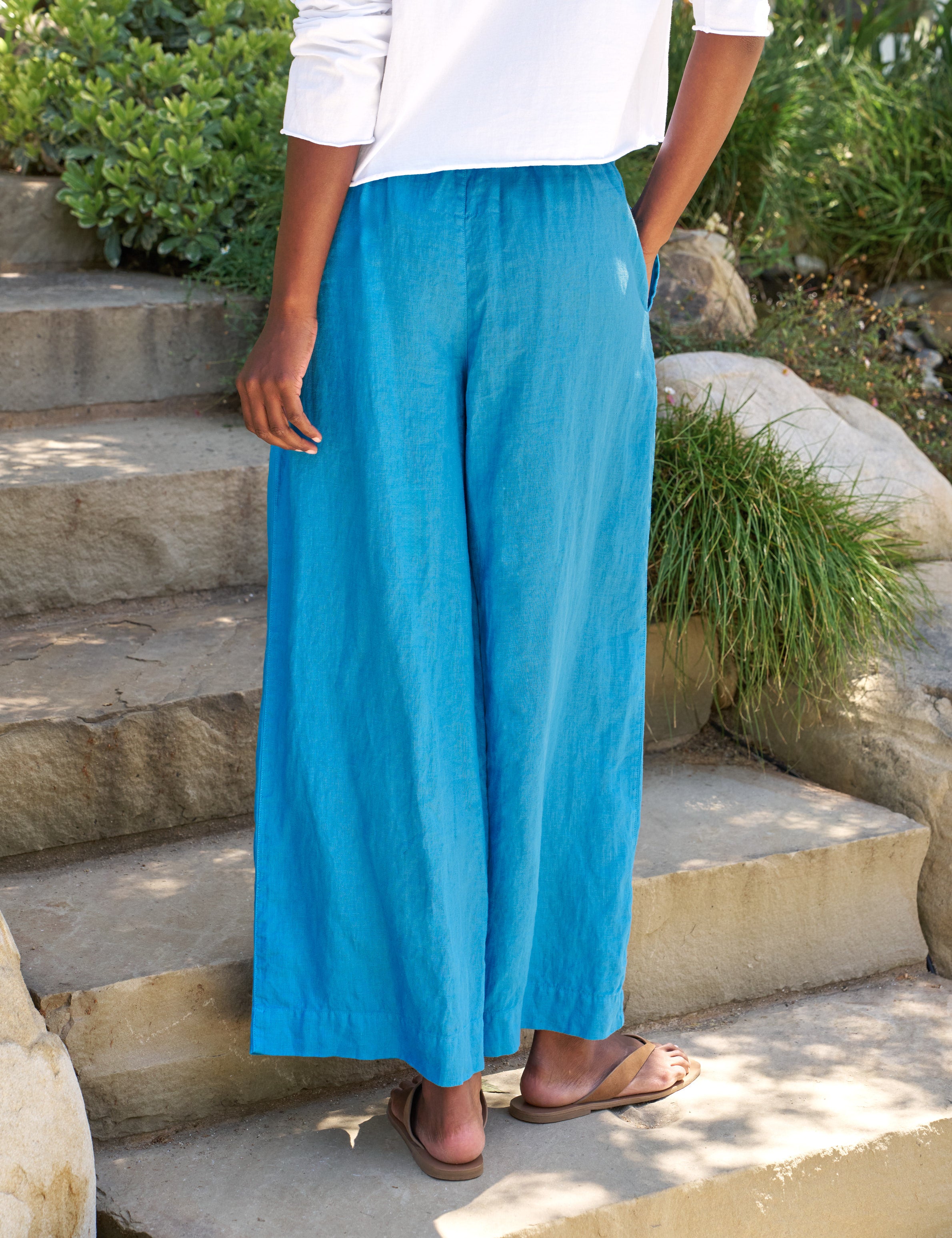 Person wearing blue pants and a white top standing on stone steps with greenery in the background, alternate view