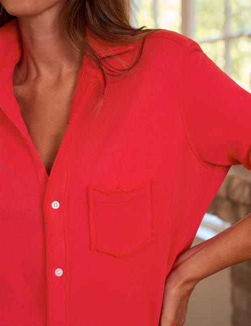A close-up of a woman wearing a bright red long-sleeve button-up shirt with a chest pocket, photographed indoors near a window., view 3