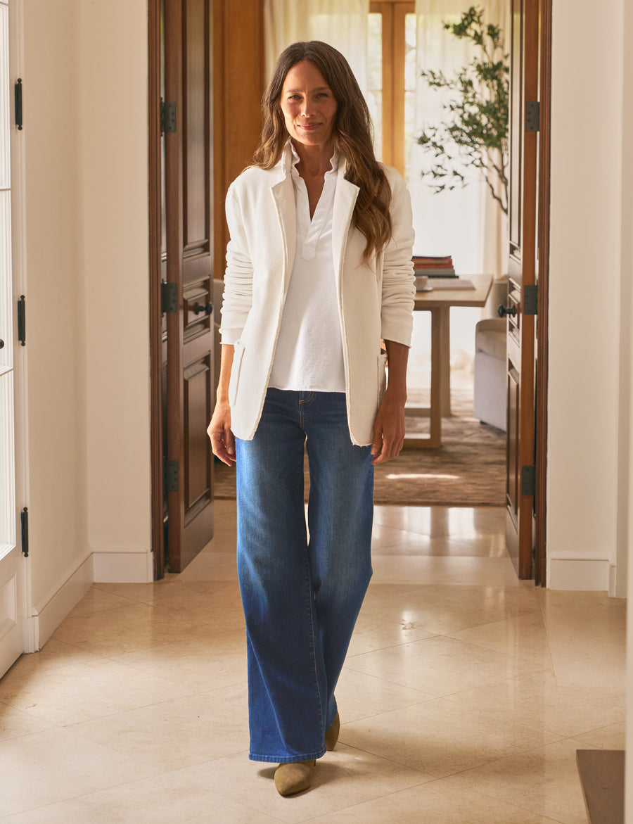 Woman wearing a white blouse and blue jeans standing in a home interior.