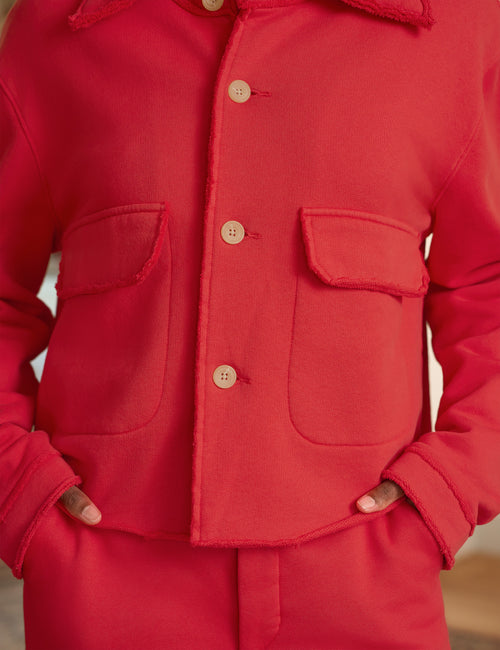 A close-up of a bright red jacket with a button-front closure, flap chest pockets, and a matching red garment worn underneath, shown on a person with hands in pockets., view 3