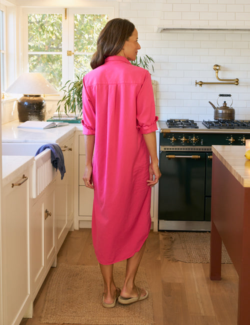 Woman in a bright pink dress standing in a kitchen., alternate view