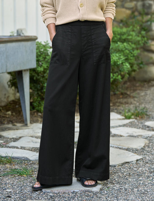 Person wearing black wide-leg pants and a beige cardigan standing outdoors., front view