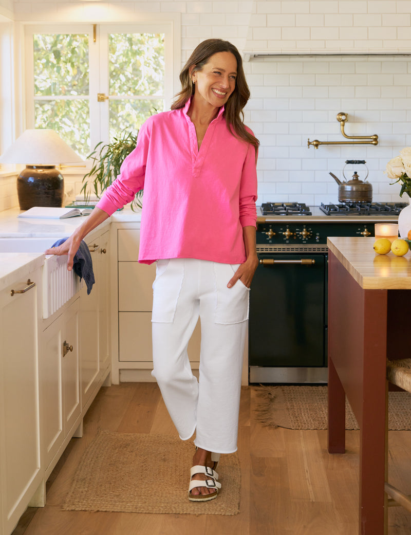 Woman in a bright pink shirt and white pants standing in a kitchen.