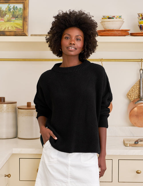 Woman wearing a black sweater and white skirt in a kitchen setting, front view