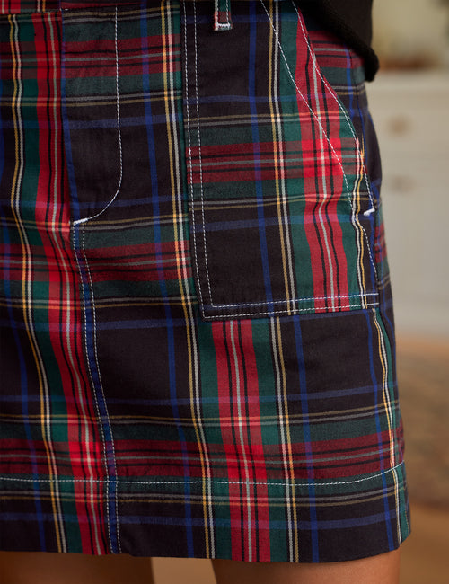 Close-up of a tartan plaid skirt with red, green, blue, and yellow stripes on a dark navy base, featuring a front patch pocket and white contrast stitching., view 3