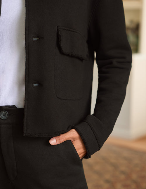 Close-up of a person wearing a black jacket over a white shirt and black trousers, with one hand in the trouser pocket., view 3