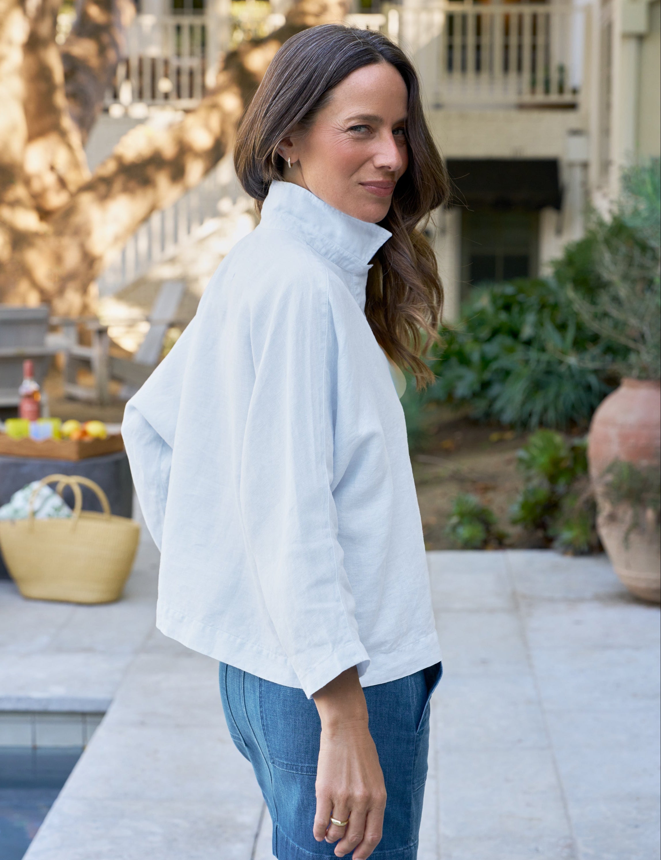 Woman wearing a light blue shirt and blue jeans standing by a pool.