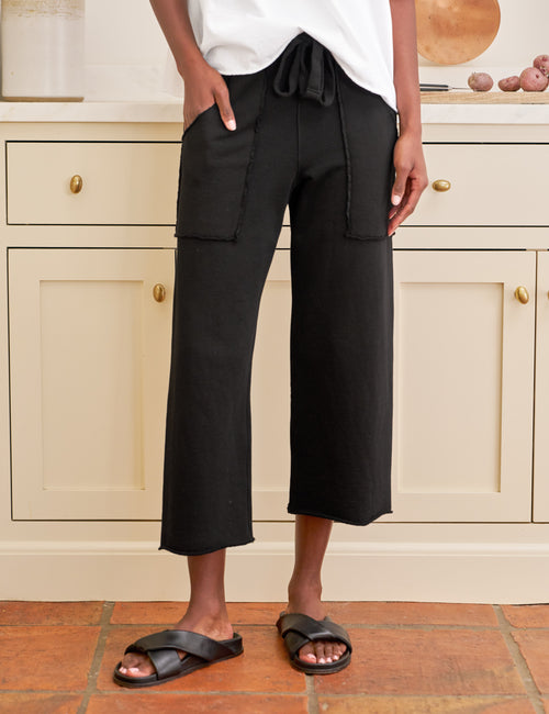 Person wearing black wide-leg pants and white top in a kitchen setting, front view