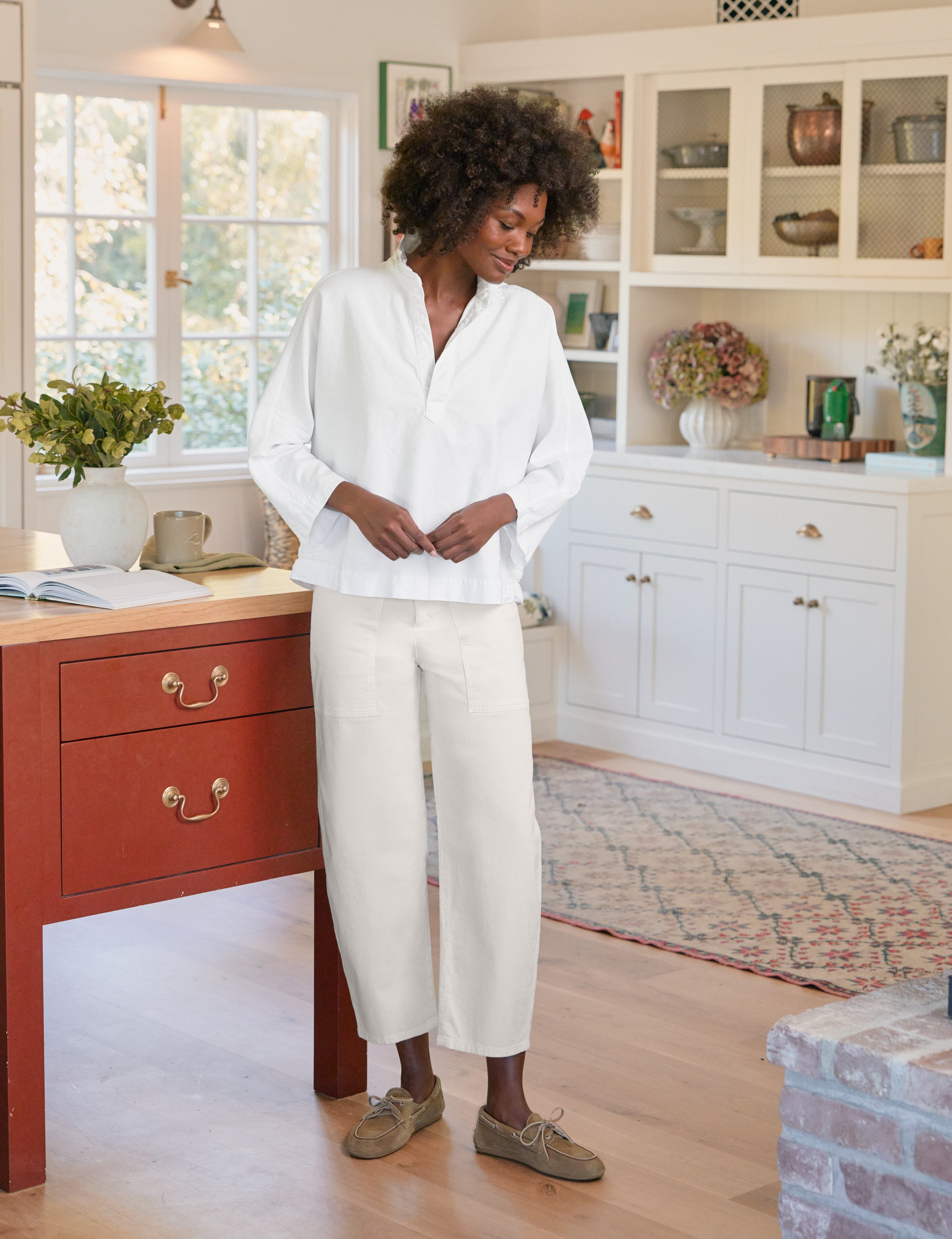 Woman in a white shirt and beige pants standing in a home office.