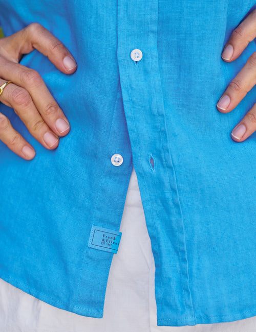Close-up of a blue shirt with a brand label, showing hands adjusting the collar., view 3