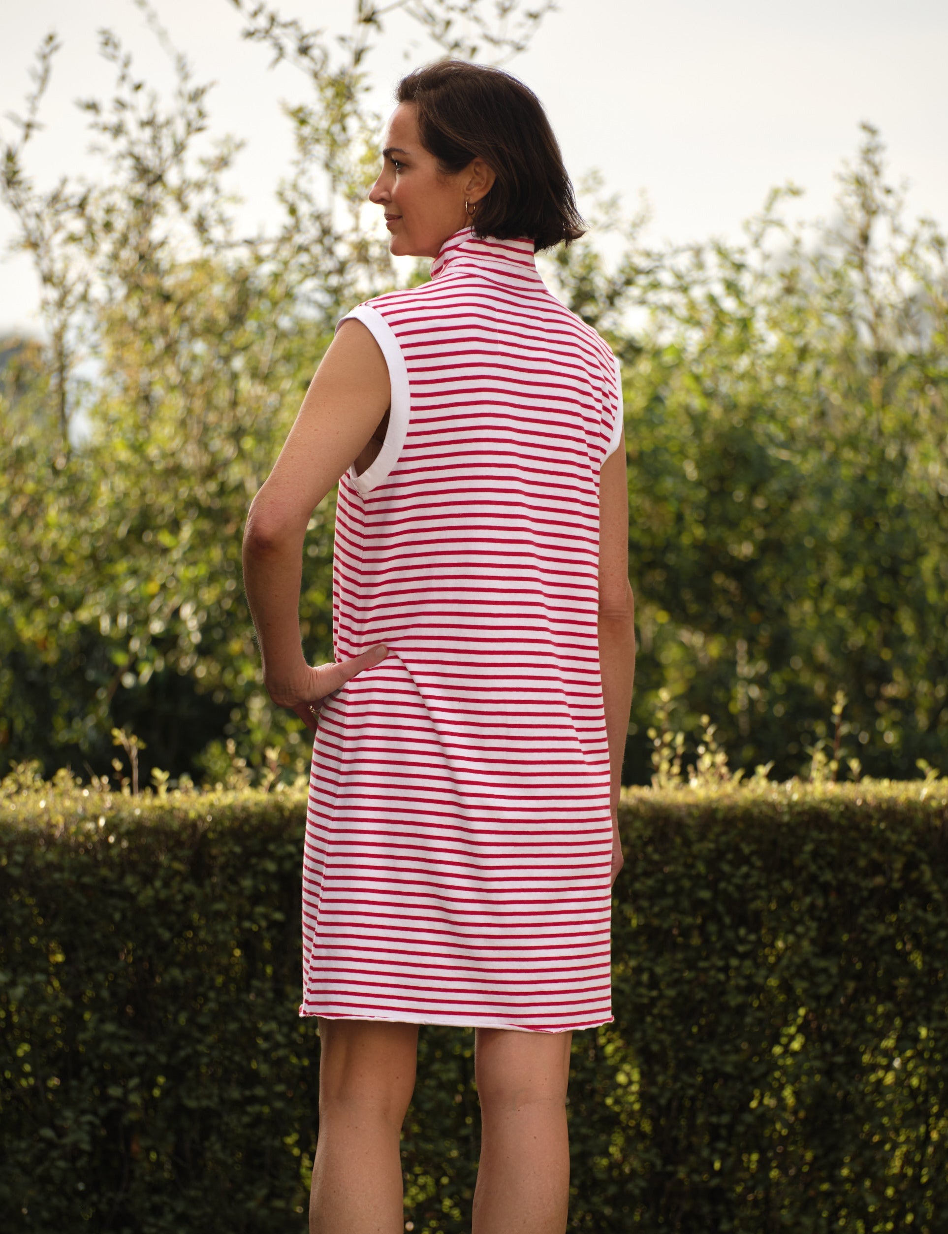 Woman wearing a red and white striped dress standing outdoors with greenery in the background, alternate view