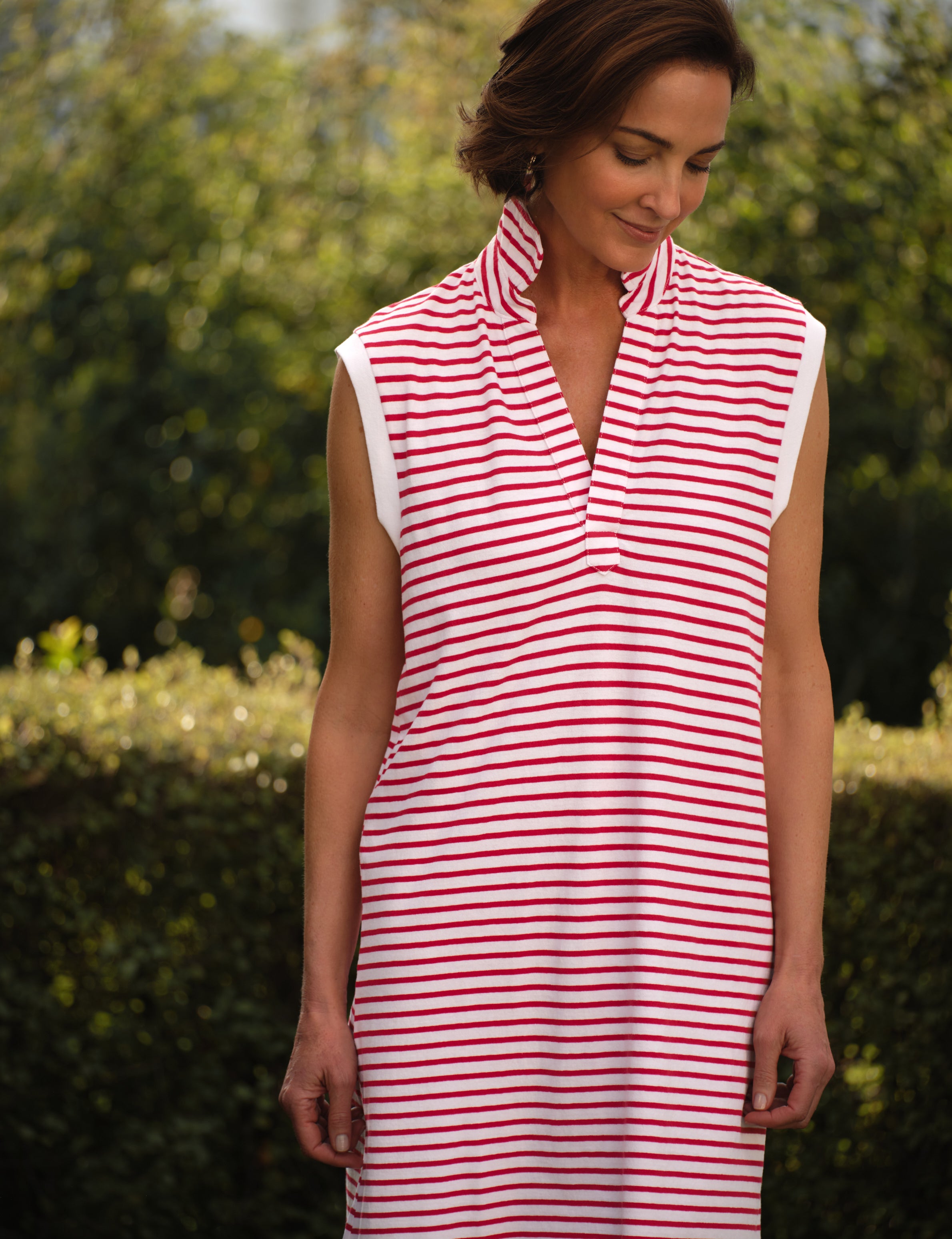 Woman wearing a red and white striped dress outdoors with greenery in the background, view 3