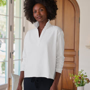 Woman wearing a white long-sleeve shirt standing in a room with a wooden door and a vase of flowers.