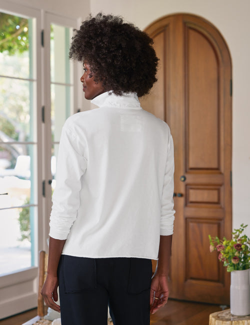 Person wearing a white shirt standing in a room with wooden doors and a plant., alternate view
