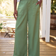 Person wearing green wide-leg pants on a wooden deck