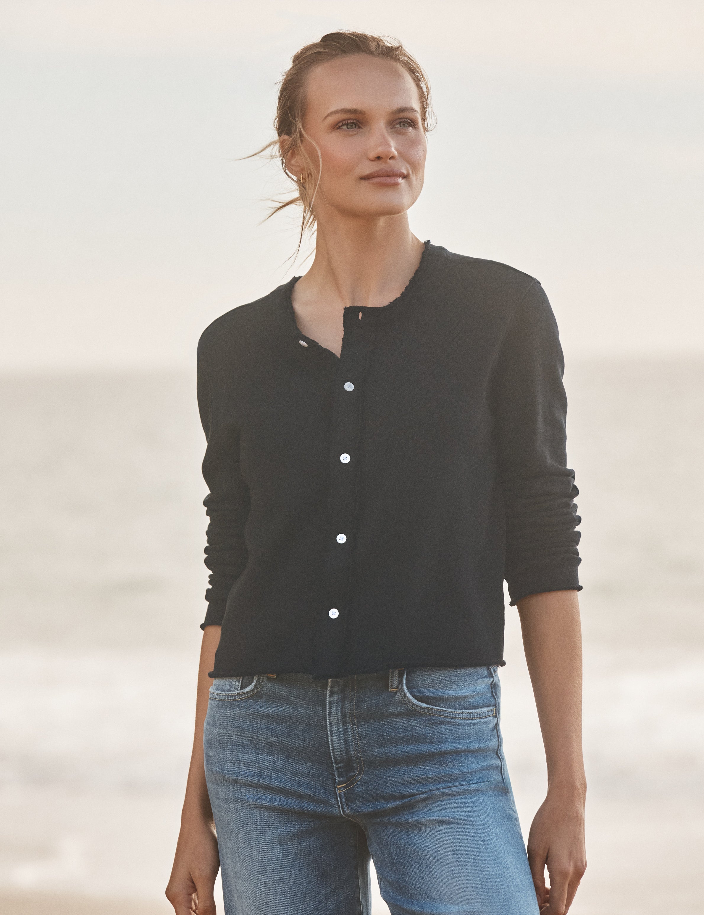 Woman wearing a navy cardigan and blue jeans standing against a light background, front view
