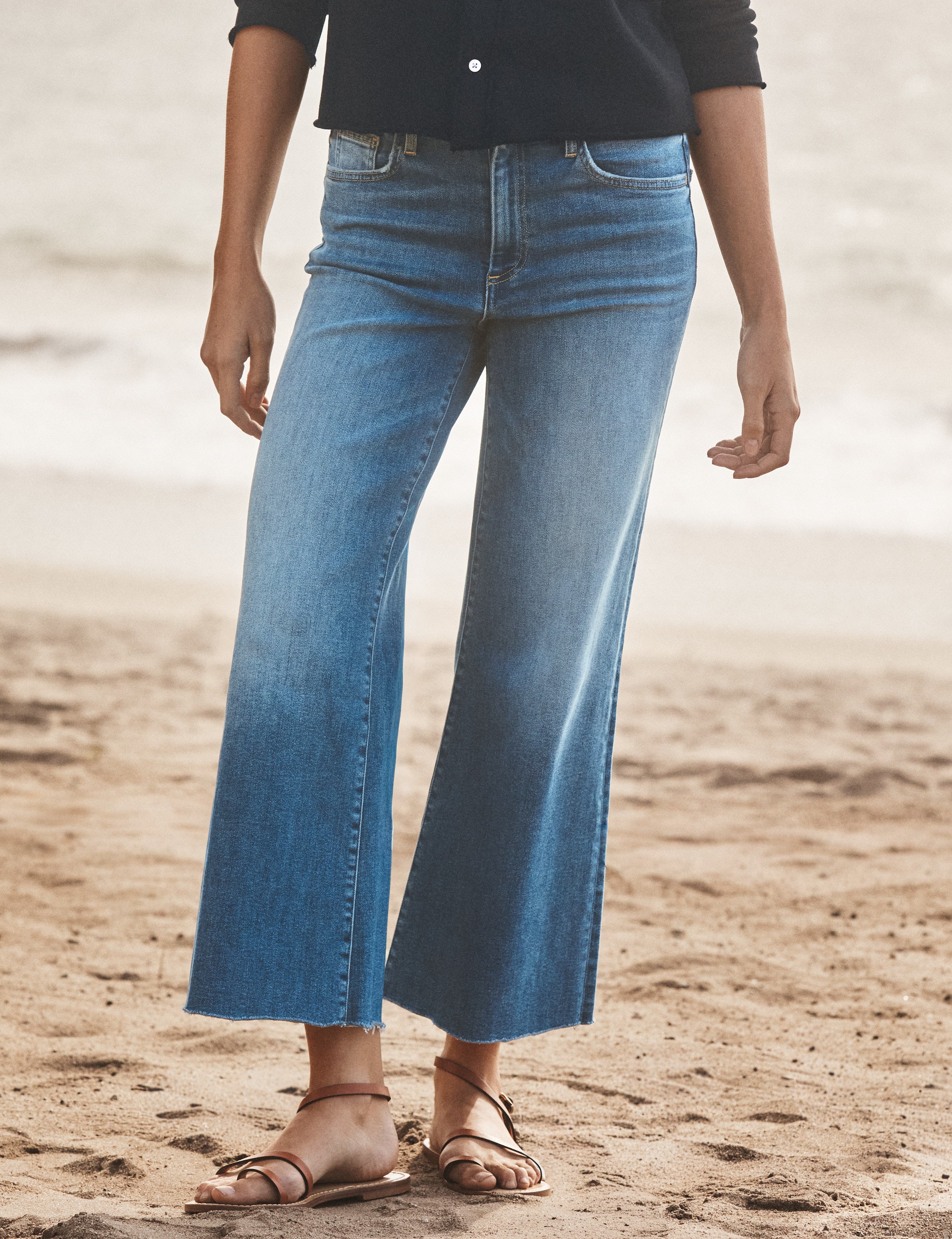 Person wearing blue jeans and a navy top on a sandy beach., front view