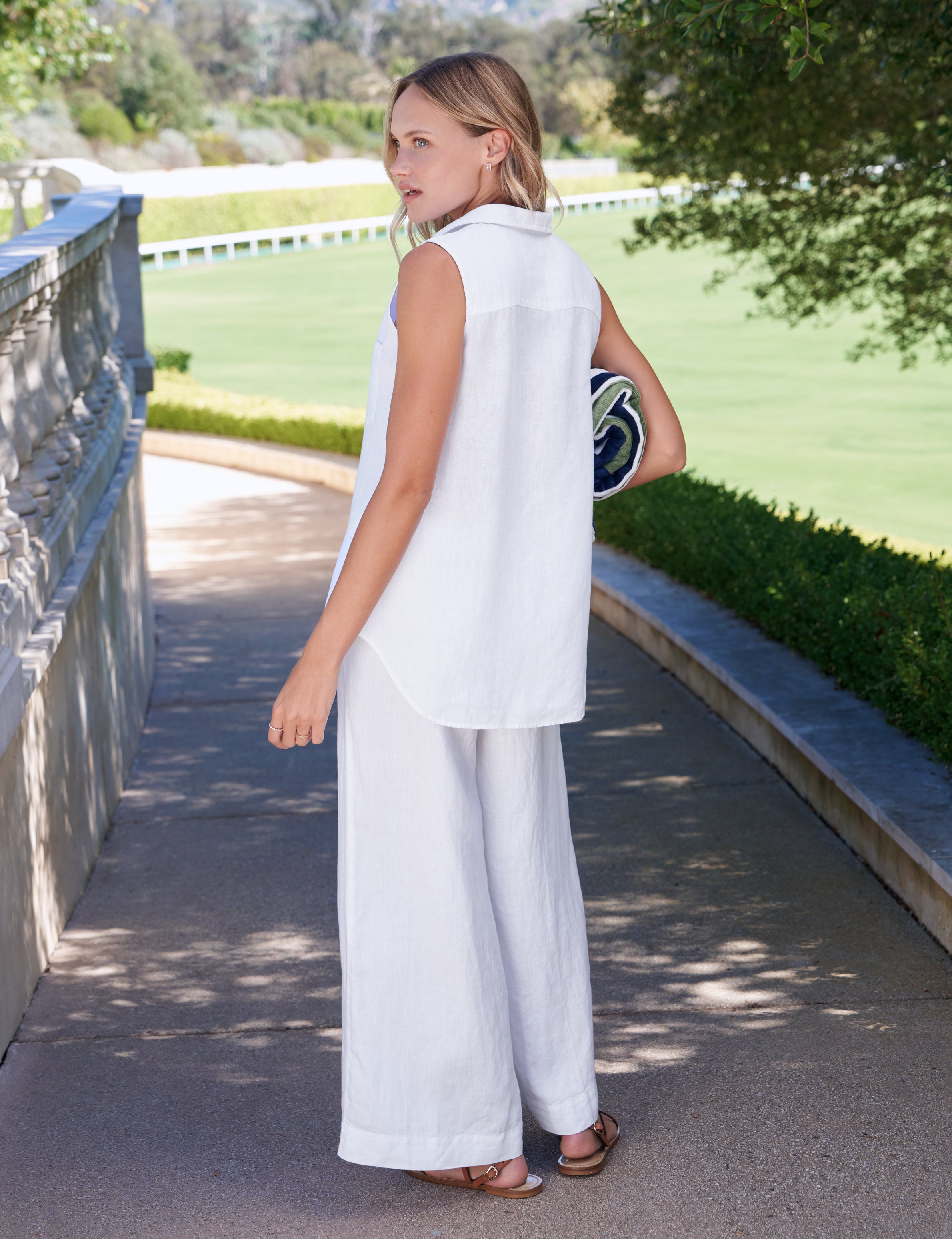 Woman in a white outfit standing on a path with greenery in the background