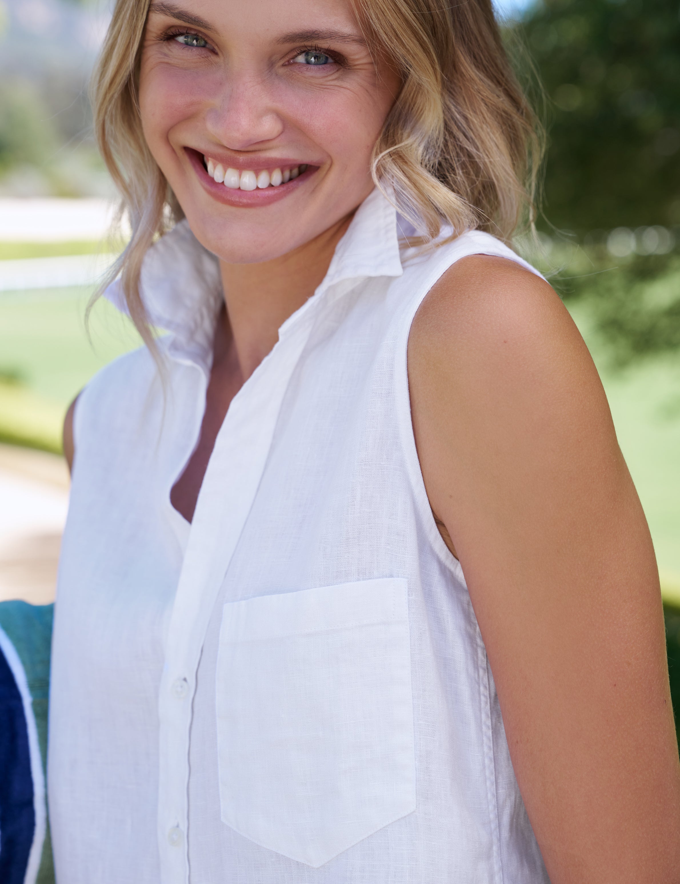 Woman wearing a white sleeveless shirt with a blurred outdoor background