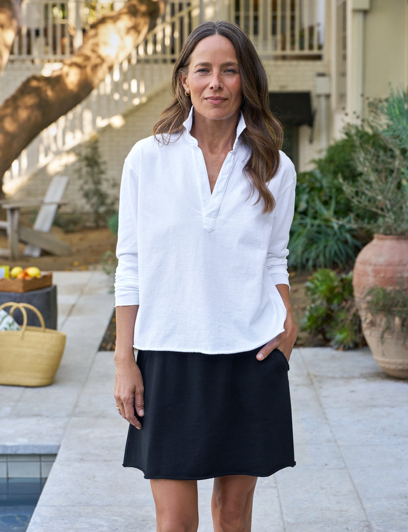 Woman wearing a white blouse and navy skirt standing outdoors.