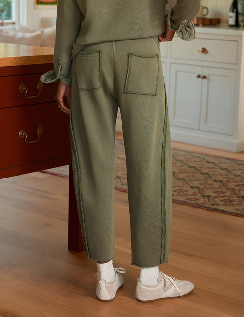 A person shown from the back wearing ribbed sage green cropped pants with large patch pockets, a matching sage green top, white socks, and white sneakers in a home interior with wood floors and cabinetry., alternate view