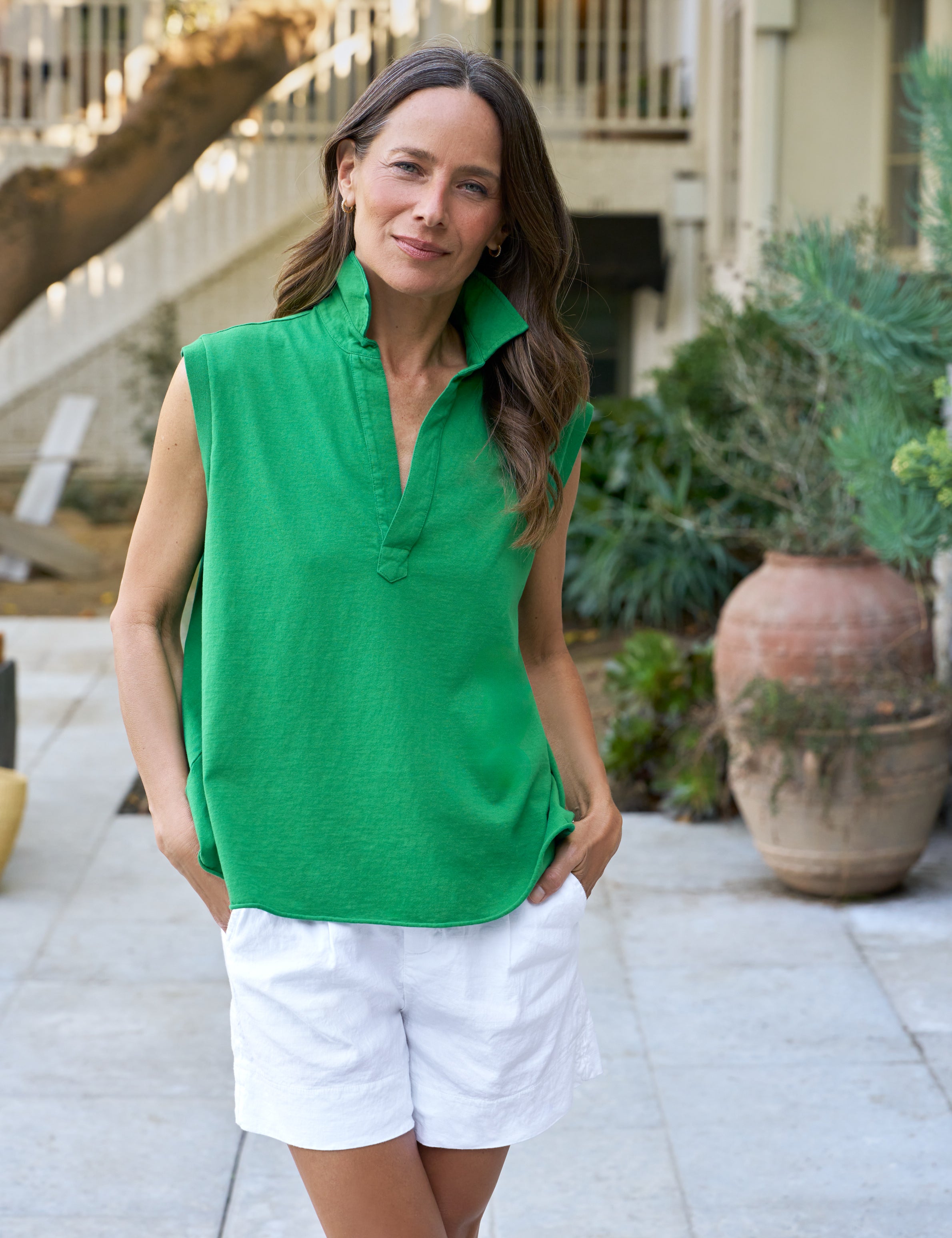 Woman wearing a green sleeveless top and white shorts standing outdoors.