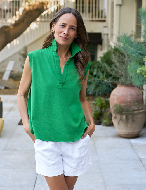 Woman wearing a green sleeveless top and white shorts standing outdoors., front view
