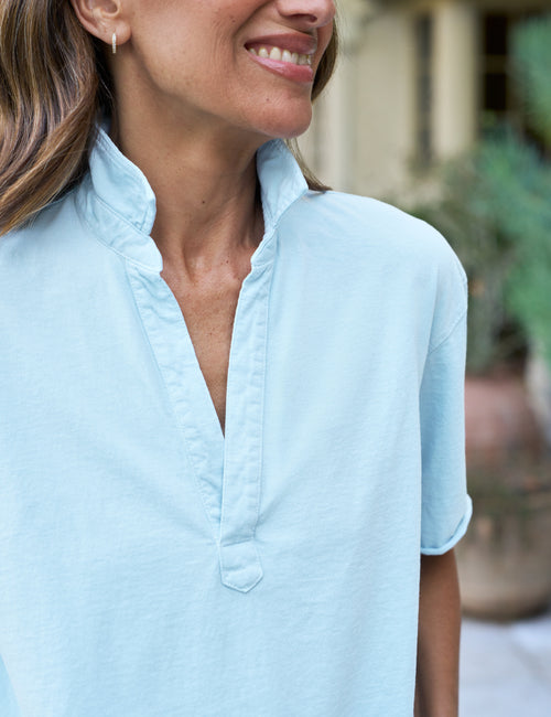 Woman wearing a light blue shirt with a blurred outdoor background, view 3