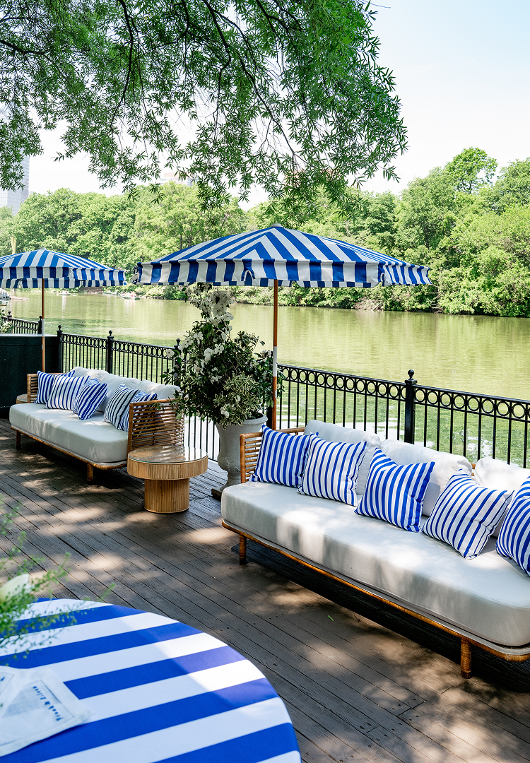 Outdoor seating area with striped umbrellas and cushions by a lake