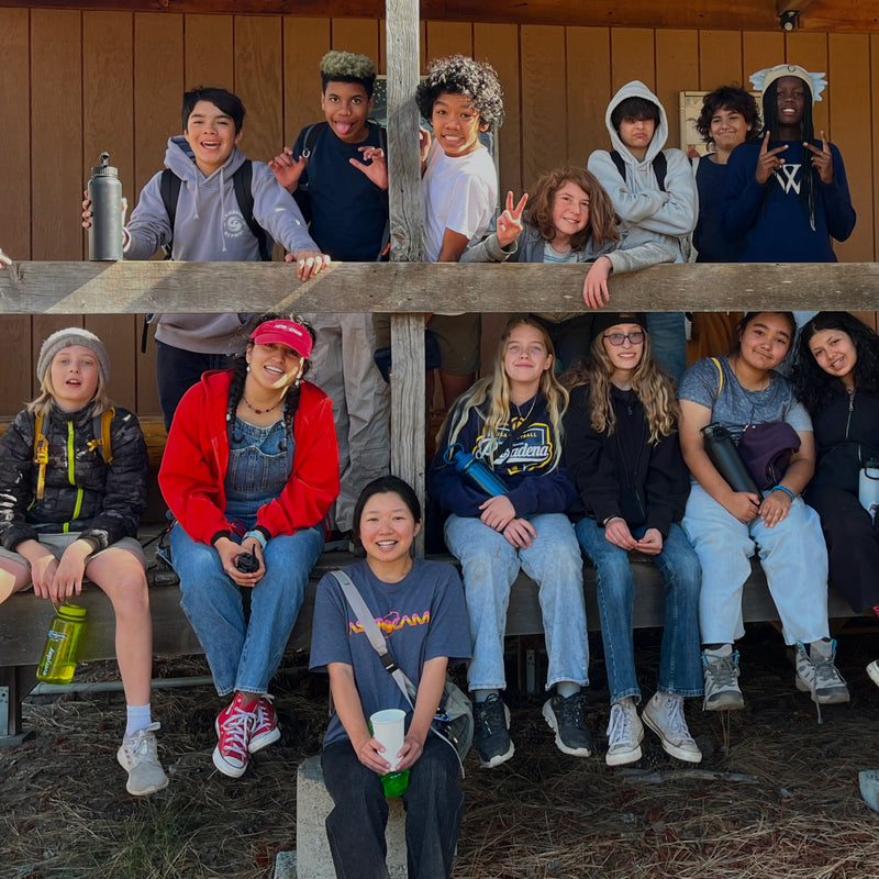 Group of people sitting on a wooden bench outdoors, posing for a photo.