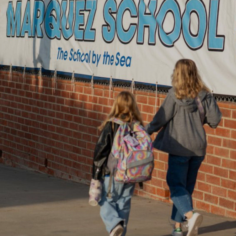 Two children walking past a school sign for Marquez School by the Sea.
