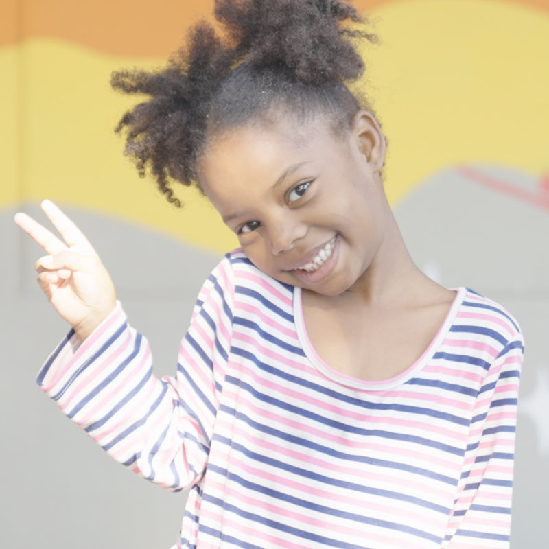 Young girl in a striped shirt making a peace sign with her hand against a yellow and gray background