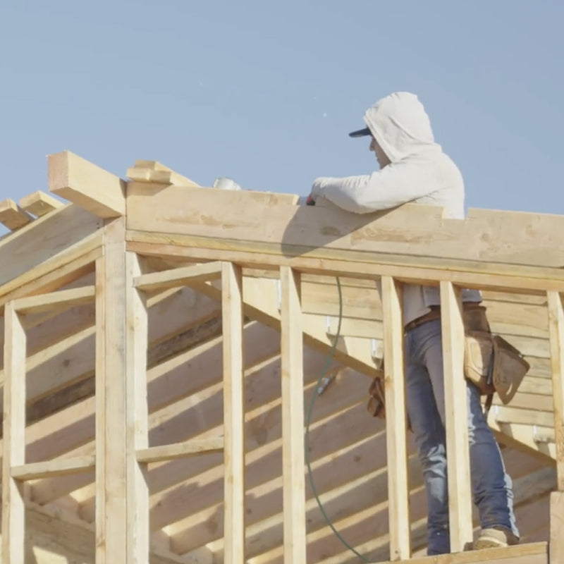 Person working on a wooden roof structure against a clear blue sky