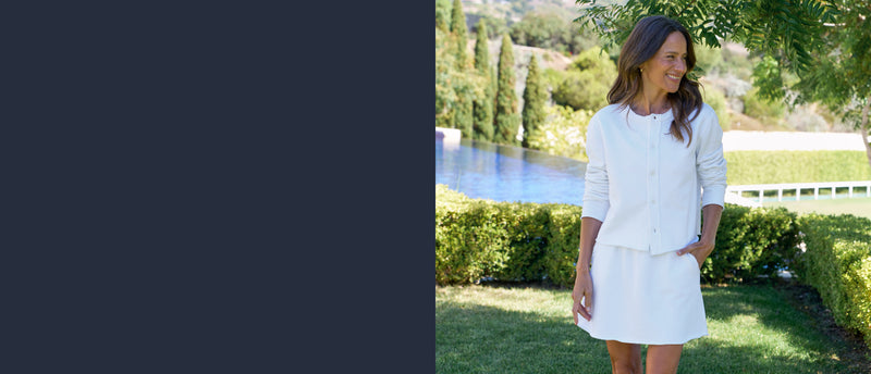 Woman in a white outfit standing by a pool with greenery in the background