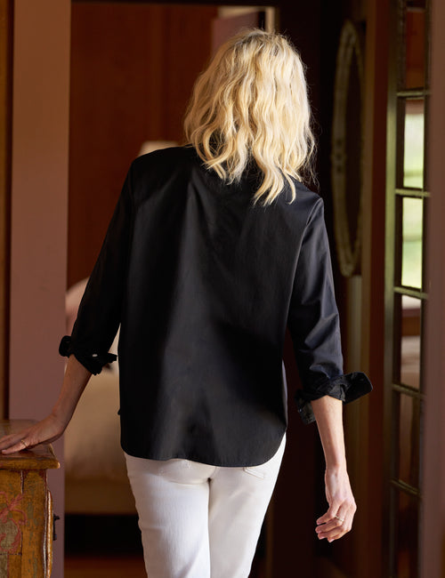 Person wearing a black blouse with rolled-up sleeves in an indoor setting, alternate view