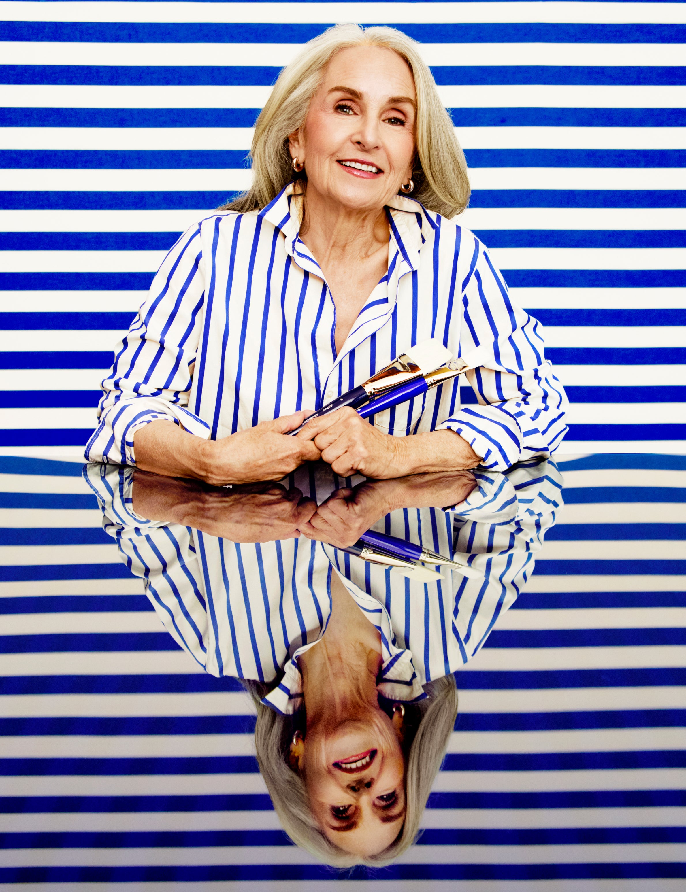 Woman in a striped shirt holding books against a blue and white striped background, front view