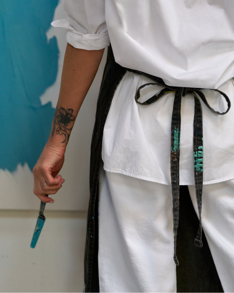 Person in white apron holding a paintbrush with a blue wall in the background