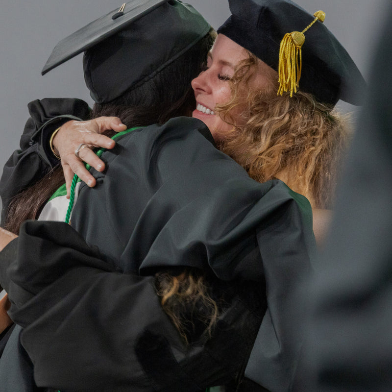 Two individuals in graduation caps and gowns embracing each other.