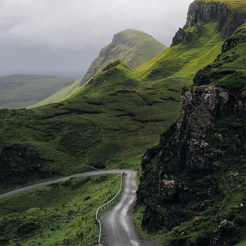 Winding road through a green, mountainous landscape on a cloudy day.