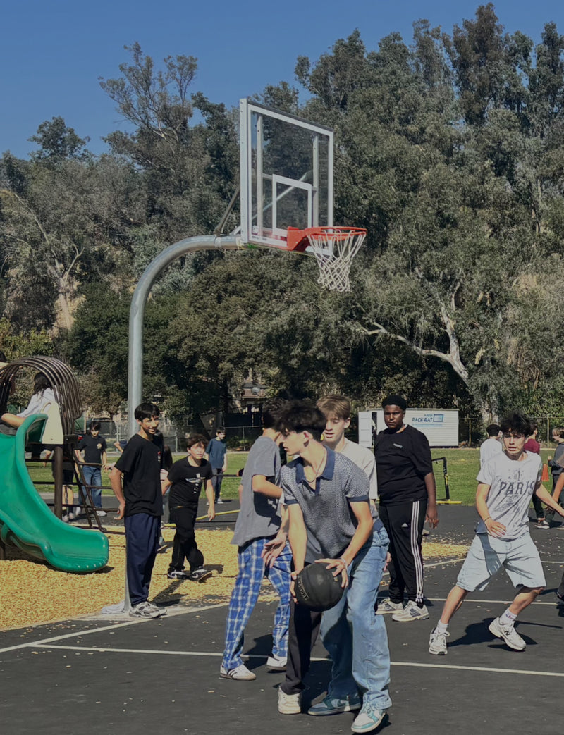 Group of people playing basketball on an outdoor court with trees in the background