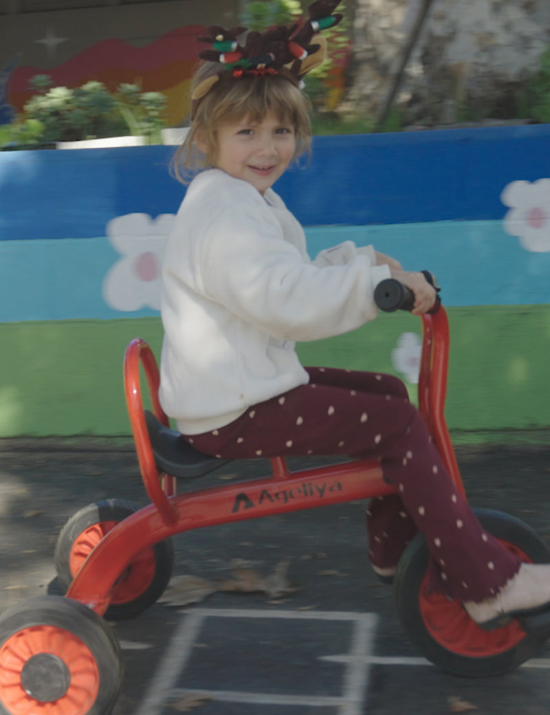 Child riding a red tricycle with a colorful background