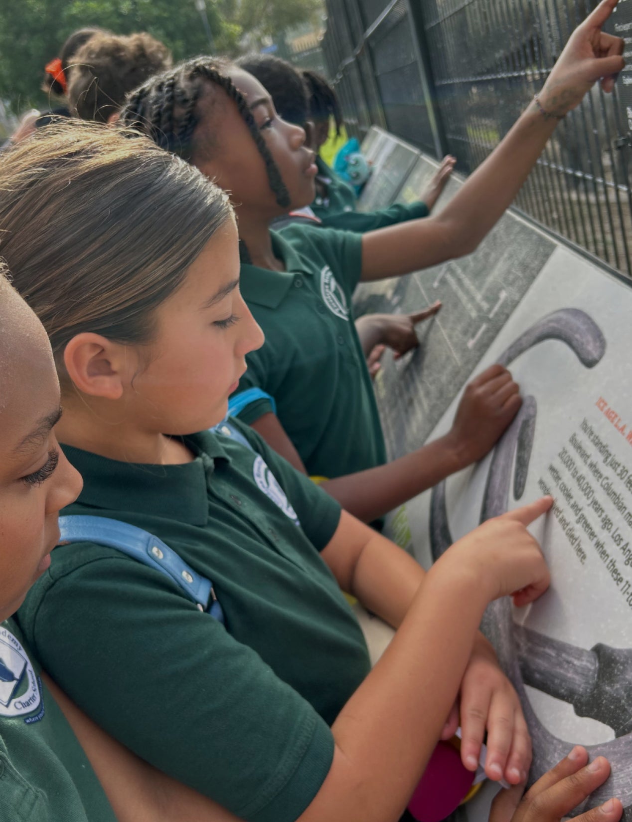 Children in green uniforms looking at a display board outdoors