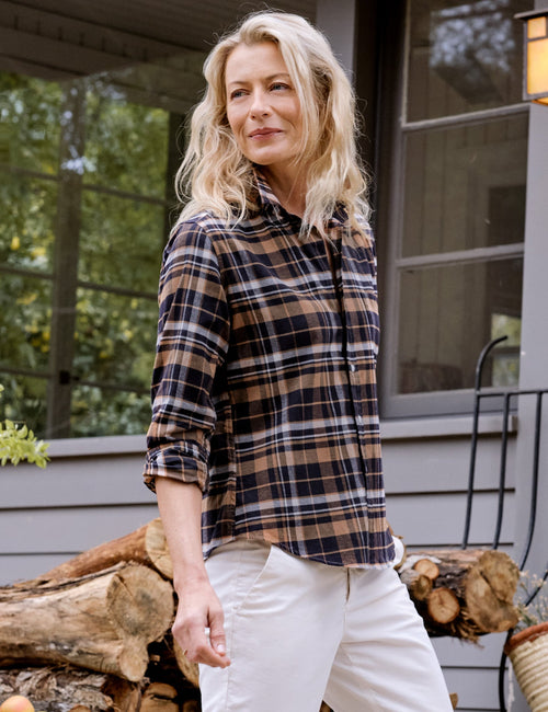 Woman standing on stone steps wearing a plaid shirt and white pants, with a basket and fruit bowl in the background., front view